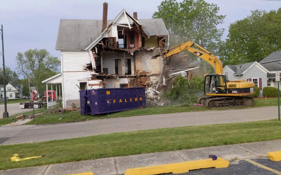 Excavadora derribando una casa junto a un contenedor roll-off morado de Falcon