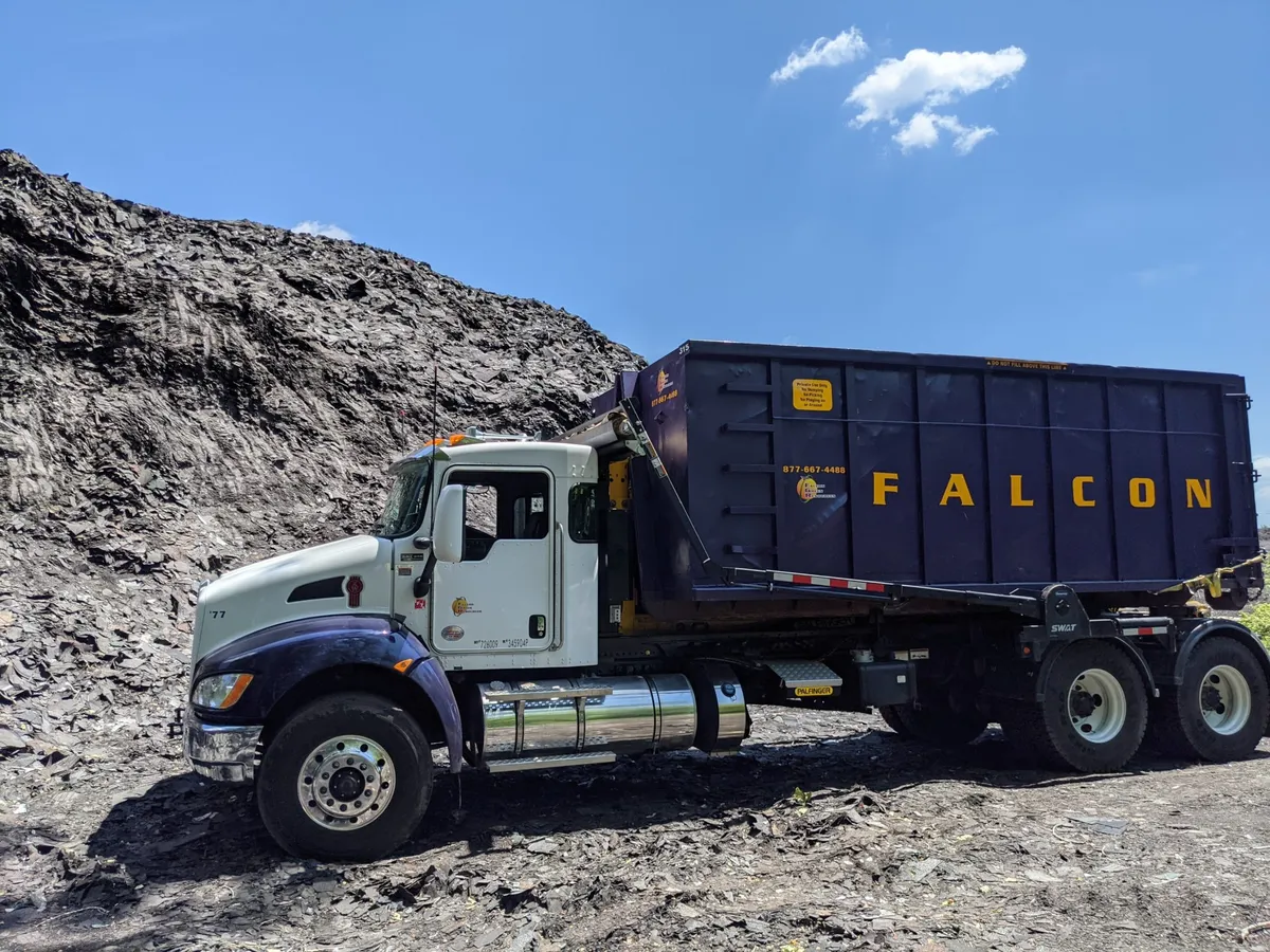 Ciężarówka roll-off Falcon Green Resources z fioletowym kontenerem obok dużej sterty materiału
