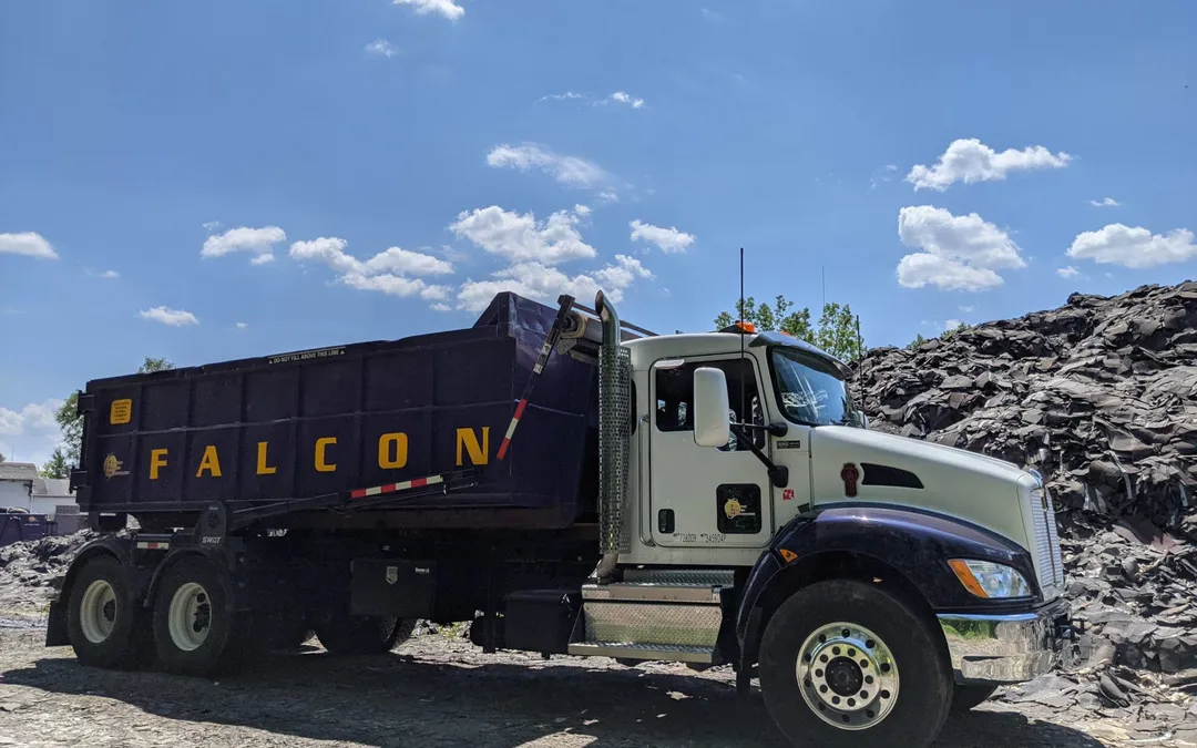 Camión roll-off de Falcon Green Resources transportando un contenedor morado frente a una gran pila de material