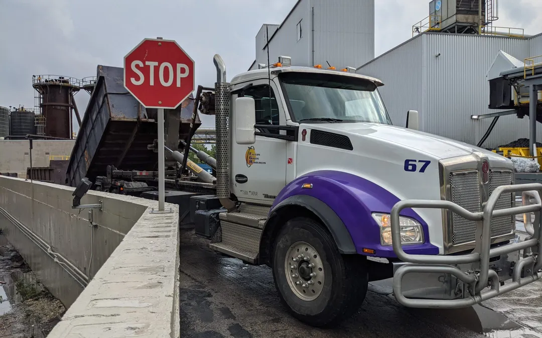 White and purple Falcon Green Resources roll-off truck, number 67, stopped at a stop sign