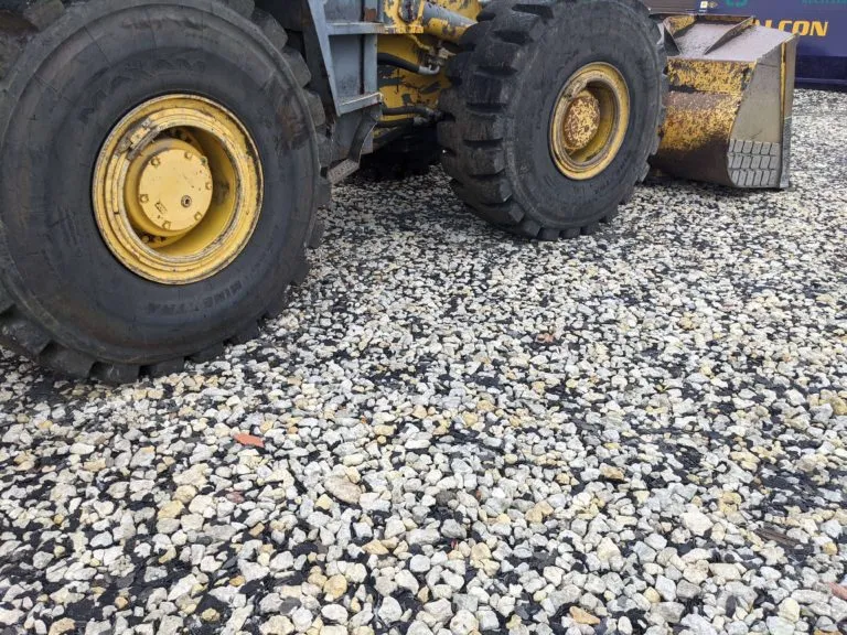 Llanta de cargador frontal sobre una superficie de piedra triturada mezclada con trozos oscuros de teja reciclada