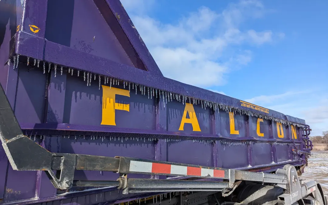 Close-up of the side of a purple Falcon Green Resources roll-off dumpster with yellow lettering and icicles along the top rail