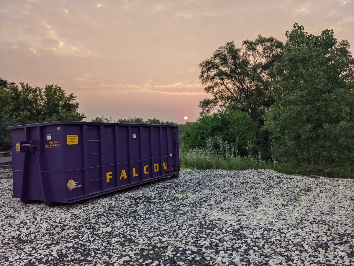 Purple Falcon Green Resources roll-off dumpster on a gravel lot at sunset