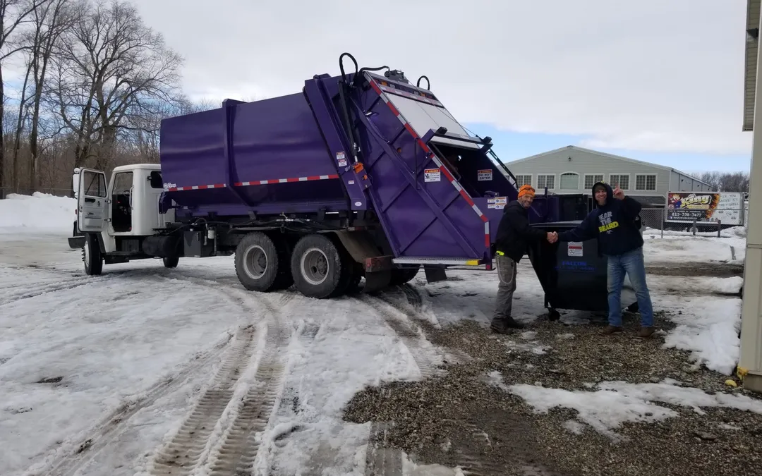 Camión de carga trasera de Falcon atendiendo un contenedor negro mientras dos personas se dan la mano en un terreno nevado