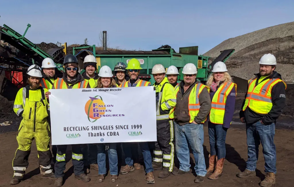 El equipo de Falcon Green Resources con cascos y chalecos de seguridad sosteniendo una pancarta que dice Illinois 1st Shingle Recycler, reciclando tejas desde 1999