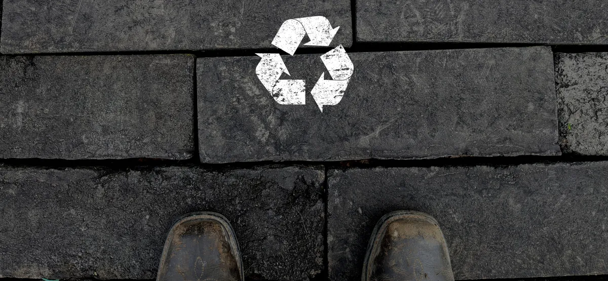 Cegły z gontów z białym symbolem recyklingu i parą butów roboczych