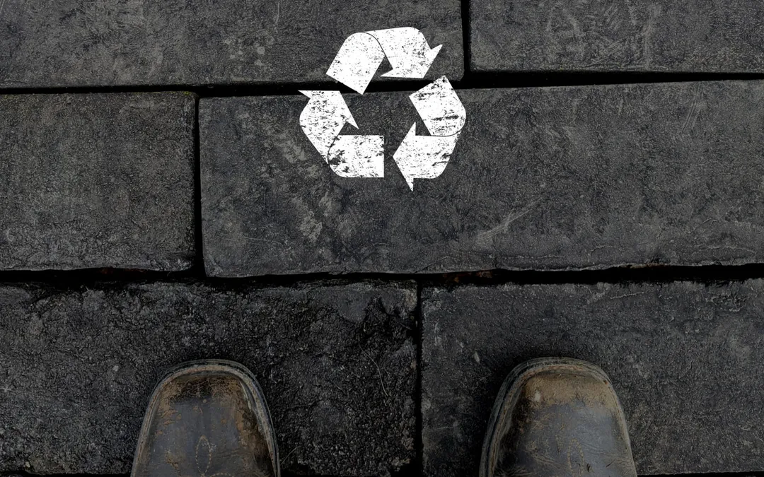 Cegły brukowe z recyklingowanych gontów oznaczone symbolem recyklingu, z butami pracownika u dołu kadru