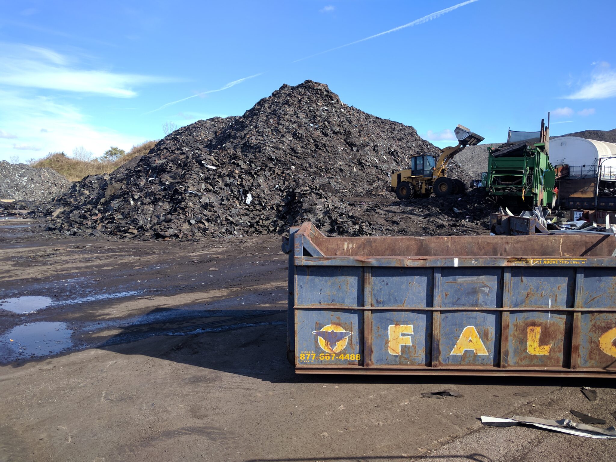 Stockpile of recovered construction material beside a Falcon roll-off container